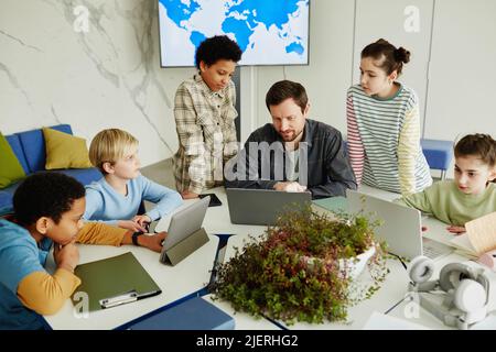 High angle view at diverse group of children with male teacher using laptops in modern school classroom Stock Photo