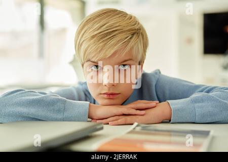 Minimal portrait of bored schoolboy lying on desk in school classroom and looking away Stock Photo