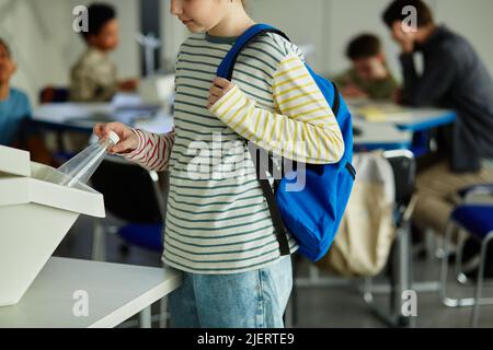 Side view of child using waste sorting bins in school and putting plastic bottle in for recycling, copy space Stock Photo