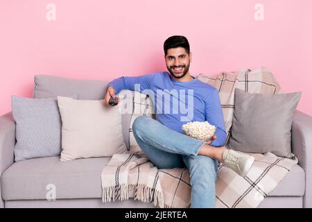 Photo of cheerful funny guy sitting couch hold pop corn bowl remote control isolated on pink color background Stock Photo
