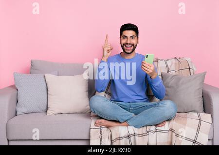 Photo of positive excited man wear long sleeve shirt sitting sofa typing modern gadget pointing empty space isolated pink color background Stock Photo