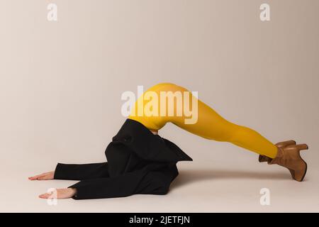 Funny portrait of young girl in yellow tights and black jacket posing, leaning on head isolated over grey studio background Stock Photo