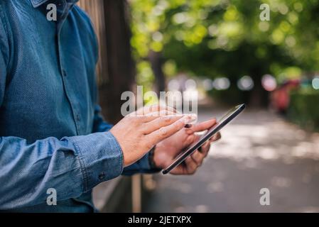 Midsection of businessman using digital tablet. Close-up of male professional commuter is wearing formals. He is standing on sidewalk in city. Stock Photo