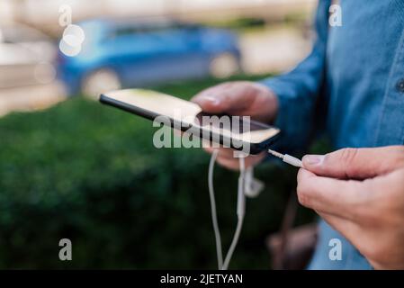 Close-up of male executive connecting headphones to smart phone. Midsection of businessman using audio equipment. He is preparing to listen music whil Stock Photo