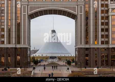 Nur Sultan (Astana), Kazakhstan, 11.11.21. Khan Shatyr Entertainment Center seen through an arch in monumental Gate, KazMunayGas JCR Stock Photo