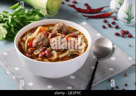 Asian spicy soup with meatballs, beans and noodles on white bowl on blue background Stock Photo