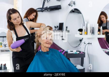 Hairdresser drying hair of elderly female Stock Photo