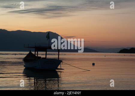 Incredible sunset over the sea, with small boats and the hills in the background, in Caieira da Barra do Sul, Stock Photo