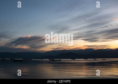 Incredible sunset over the sea, with small boats and the hills in the background, in Caieira da Barra do Sul, Stock Photo