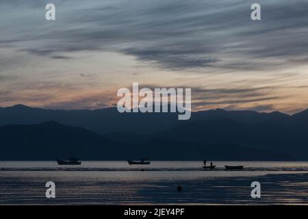 Incredible sunset over the sea, with small boats and the hills in the background, in Caieira da Barra do Sul, Stock Photo