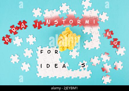 Puzzle on a blue background, yellow crumpled paper, words brainstorming for ideas are standing on the jigsaw pieces, business concept, working as a te Stock Photo