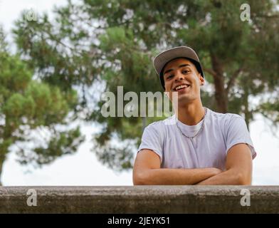 Low angle shot of a smiling guy with cap and arms grossed looking down Stock Photo