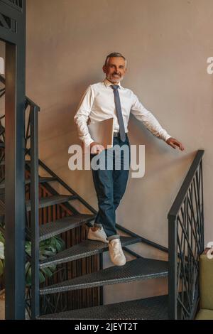 Man with laptop walking down stairs looking at camera Stock Photo