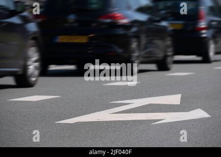 Dark cars drive one after the other in a lane on an asphalt street. The right lane with arrows straight ahead and to the right is empty. Focus on the Stock Photo