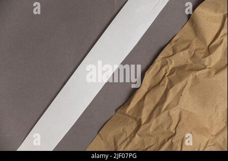 Wrapping paper and a white diagonal stripe against the gray background. Crumpled sheet of light brown paper lies on gray surface. Top view. Space for Stock Photo