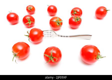 Separated cherry tomatoes distributed on a white background. One tomato is pierced with a tiny fork. Stock Photo