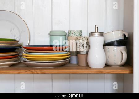 Wooden shelf with kitchen utensils, rustic style. Tableware, plates and cups stand on a shelf in the kitchen. Cupboard with set of colourful dishes, m Stock Photo