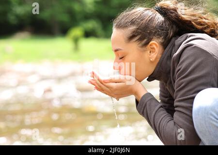 Side view portrait of a woman drinking water from river in the mountain Stock Photo