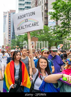 A woman of Asian descent holds a sign reading 'Abortion Is Healthcare' as she marches during Pride Parade. Stock Photo