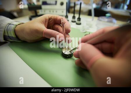 Close-up of unrecognizable watchmaker in finger gloves using tweezers and lubricating watch movement Stock Photo