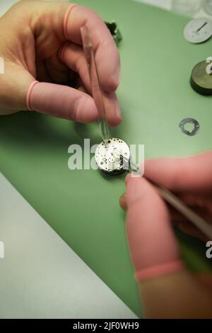 Close-up of unrecognizable engineer in pink finger gloves using dropper and tweezers while adding lubricant into watch movements Stock Photo