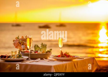 Romantic sunset dinner on the beach. Table honeymoon set for two with luxurious food, glasses of champagne drinks in a restaurant with sea view Stock Photo