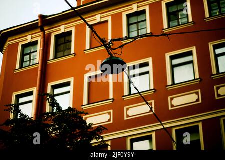A view from below of the facade of an old vintage red building and an unlit street lamp. A house in the European capital. Tourism and travel. Stock Photo