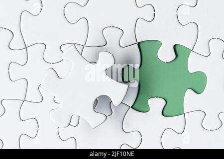 White jigsaw puzzle with missing piece on green background. Copy space. Stock Photo