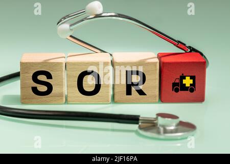 Red Inscription in Polish SOR 'hospital emergency department' on wooden blocks, a medical stethoscope and an ambulance symbol, Health concept in Polan Stock Photo