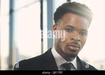 Portrait of content confident bearded African-American businessman with short curly hair standing against window Stock Photo