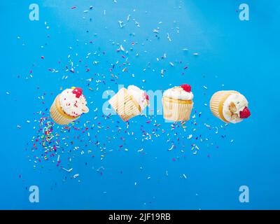 Small cupcakes with cream and fresh berries on a bright blue background in a frozen flight. Sweet food, light dessert, birthday party, banquet, picnic Stock Photo
