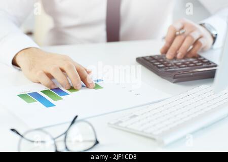 Close-up of unrecognizable male financier sitting at workplace and using calculator and graph paper while calculating profit of company Stock Photo