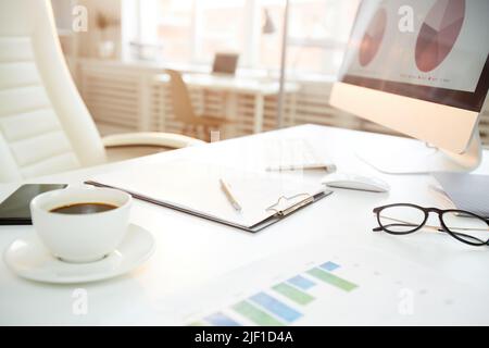Close-up of modern workplace with financial papers, coffee and computer with graphs on screen in office Stock Photo