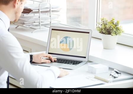 Over shoulder view of concentrated business expert sitting at desk and analyzing statistical pie chart on laptop Stock Photo