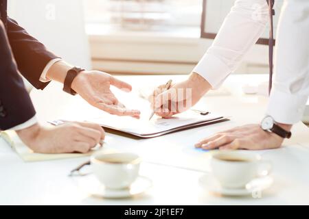 Close-up of unrecognizable business colleagues standing at table and discussing analytical points while viewing papers together Stock Photo