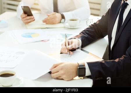 Close-up of unrecognizable business executives sitting at table and examining data in papers at annual meeting Stock Photo