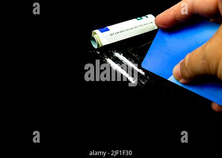 Hand holding a credit card making Two lines of Cocaine beside a wrapped up euro bill on black background Stock Photo