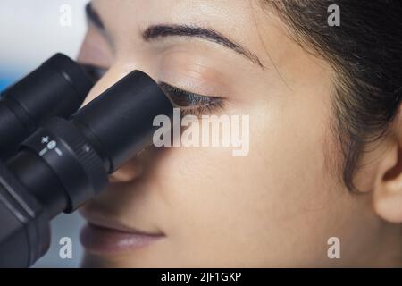 Close-up of serious young Indian researcher concentrated on scientific experiment using microscope Stock Photo