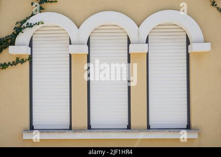 White roller shutters on narrow windows in a building. Stock Photo