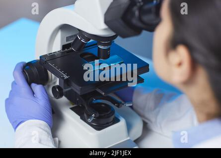Over shoulder view of unrecognizable scientist investigating sample on glass slide via microscope in laboratory Stock Photo