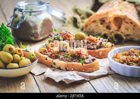 Fresh homemade chicken liver pate on ciabatta bread with roasted onions and olives on wooden table Stock Photo