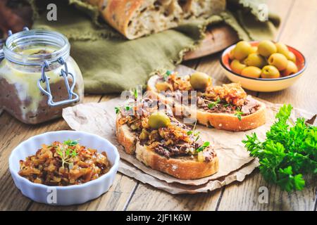 Fresh homemade chicken liver pate on ciabatta bread with roasted onions and olives on wooden table Stock Photo