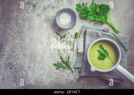 Healthy homemade green herb soup in pot made from local wild and garden herbs on grey Stock Photo