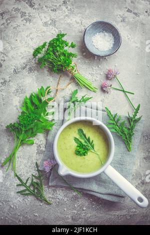 Healthy homemade green herb soup in pot made from local wild and garden herbs on grey Stock Photo