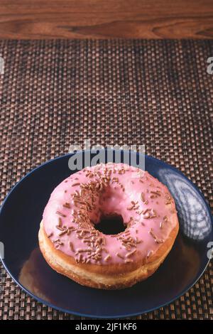 delicious round shaped bread with pink icing and colorful sprinkles on a dark plate ready for breakfast Stock Photo