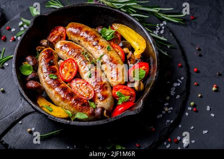 Grilled sausages and vegetables with herbs in iron pan on black background Stock Photo