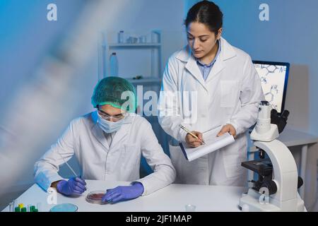 Team of young multi-ethnic clinical researchers in lab coats working with medical substances in modern laboratory Stock Photo