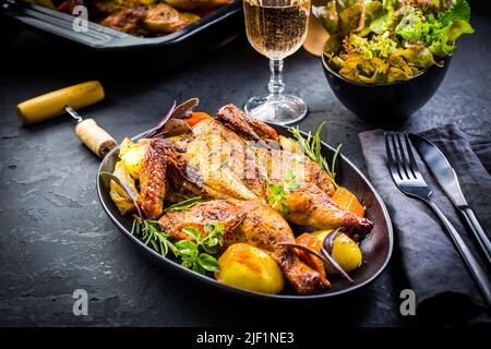 Baked whole chicken with potatoes, carrots, herbs and salt and rose wine on black background Stock Photo