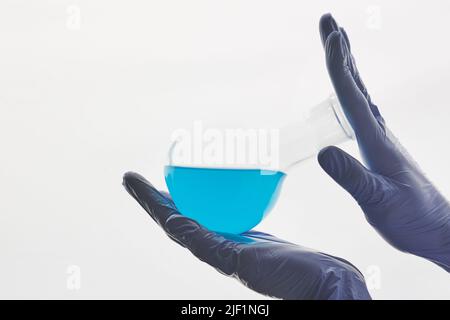 Close-up of unrecognizable laboratory worker in rubber gloves shaking beaker with blue liquid against white background Stock Photo