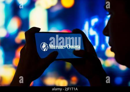 In this photo illustration, a silhouetted woman holds a smartphone with the Mutual of Omaha logo displayed on the screen. Stock Photo